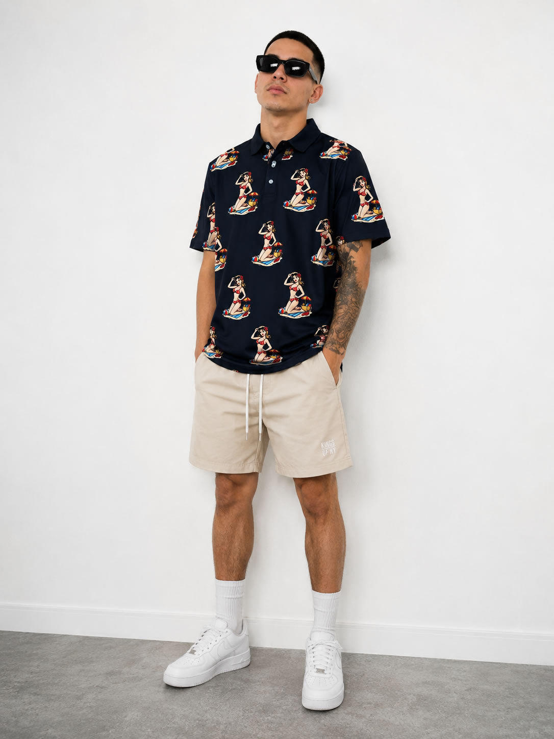 Male Model wearing Black Pin Up Girl Beach Men's Golf Polo Shirt with logo khaki shorts and sunglasses