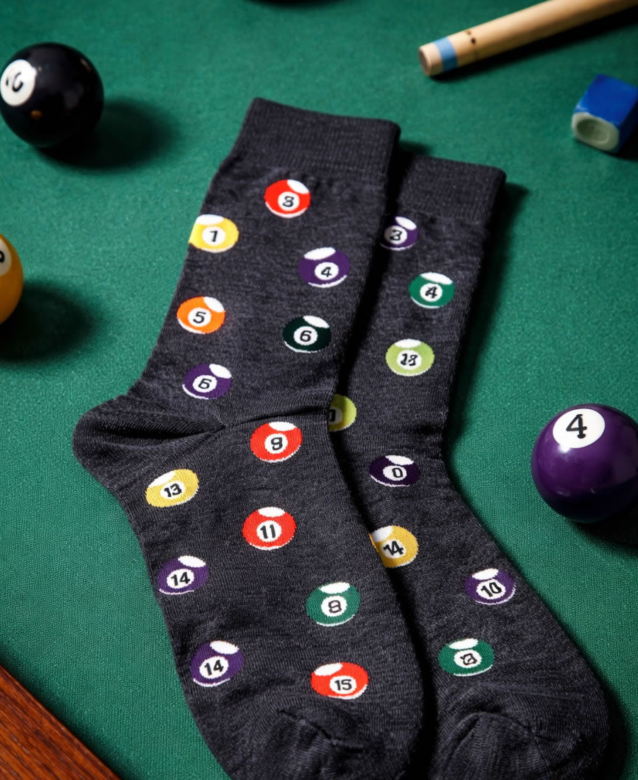 Dark gray socks with pool ball designs on a pool table with pool balls and cues.