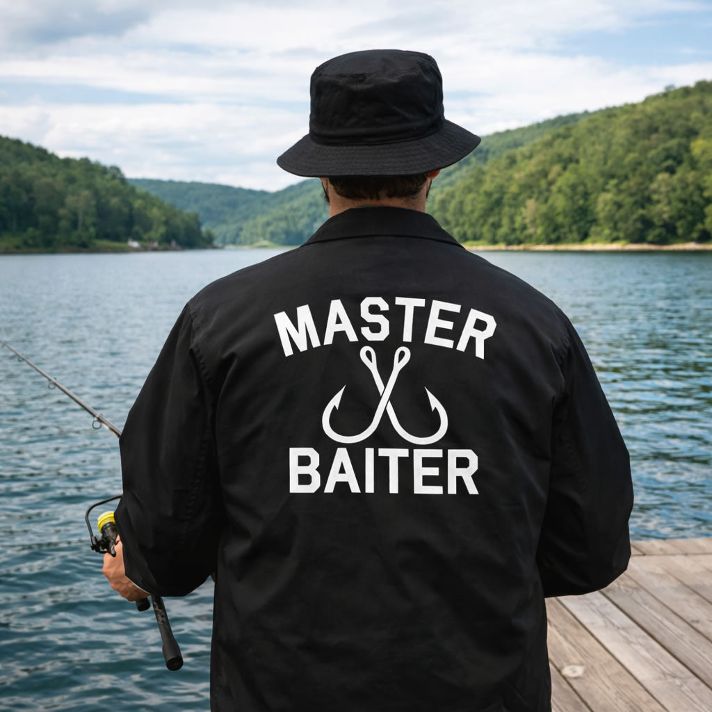 Person wearing a black jacket with 'Master Baiter' text and fishing rod by a lake