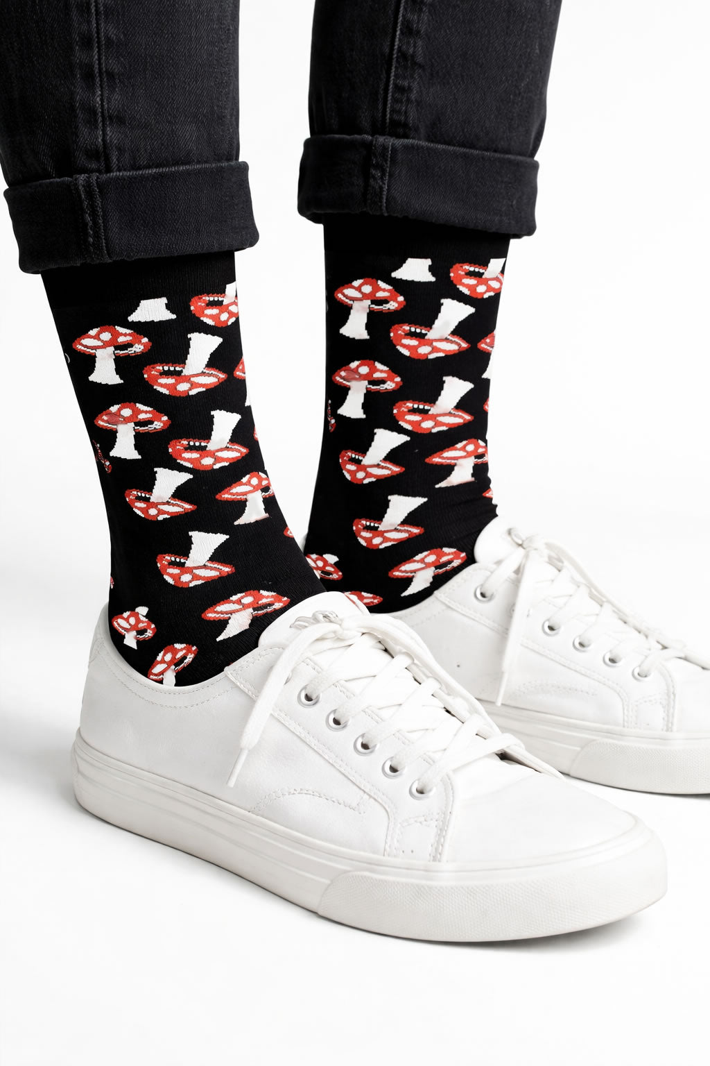 Person wearing black and red mushroom socks with fungi inspired pattern and white sneakers on