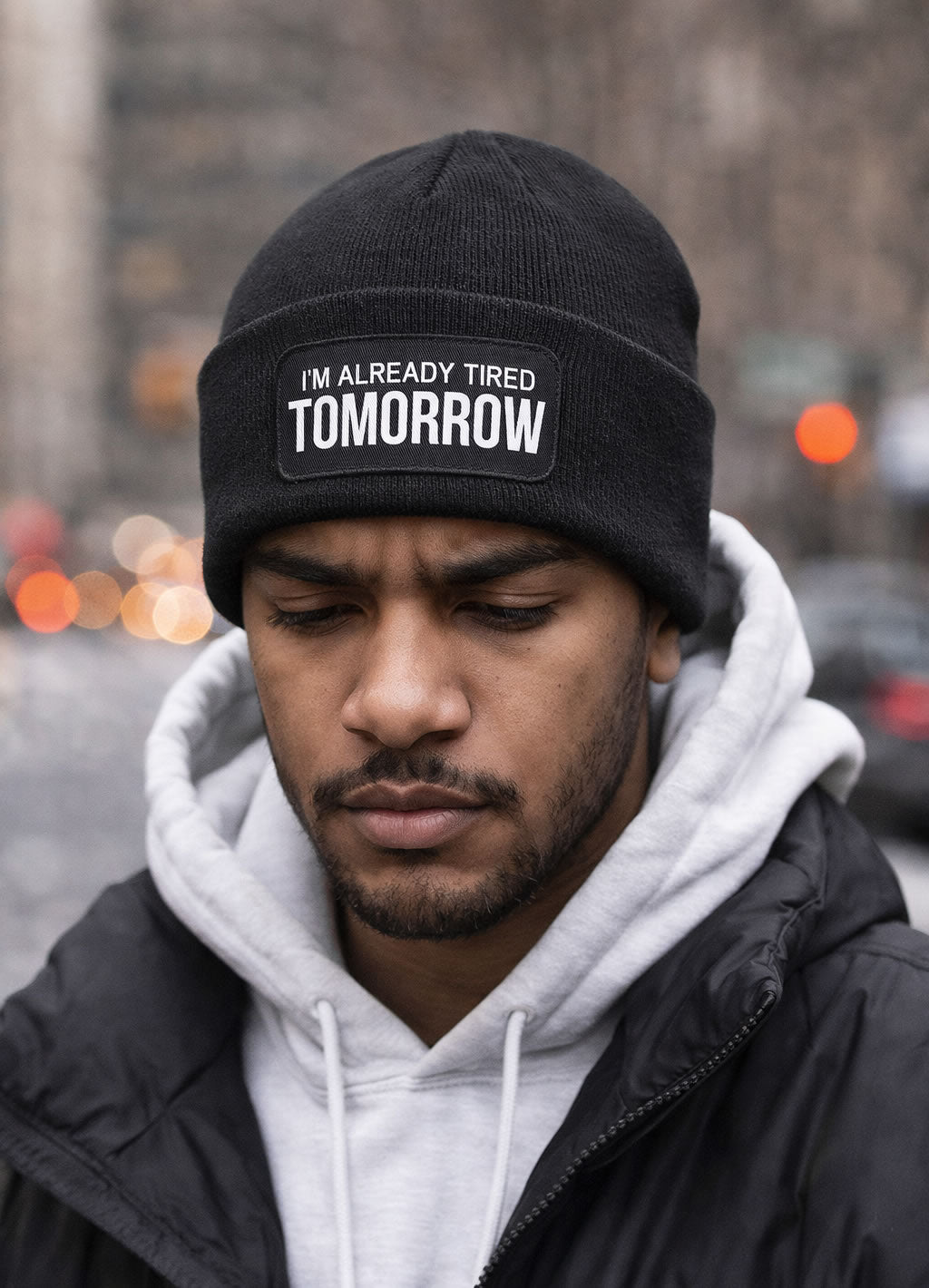 Male model wearing the I’m Already Tired Tomorrow beanie hat in a NYC streetwear setting with hoodie and jacket.
