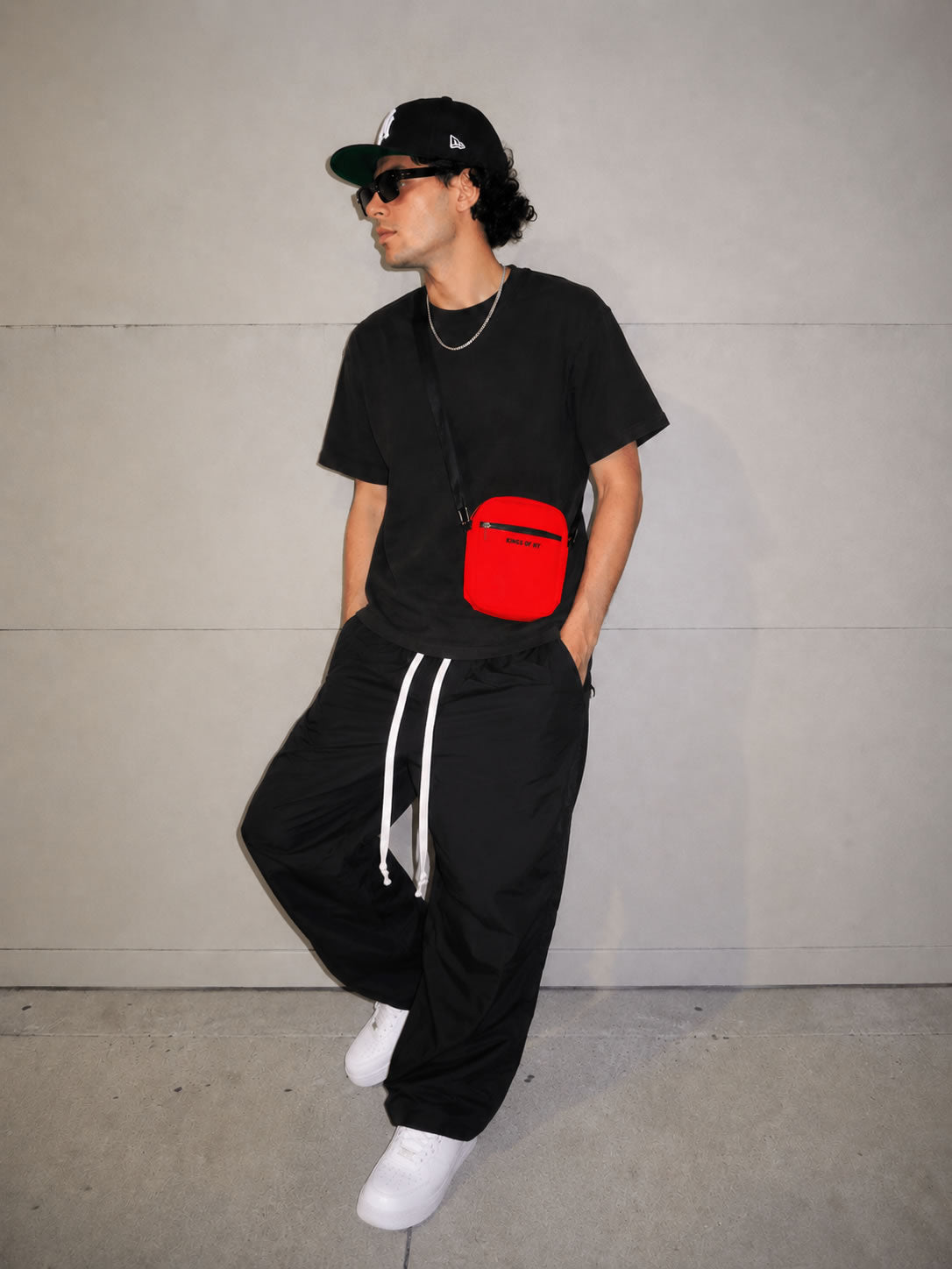 model wearing black clothing and a men's red crossbody bag by kings of ny